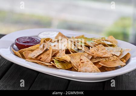 Dreieckige Nachos-Chips mit Tomatenketchup und Käsesauce auf weißem Teller und Holzboden Stockfoto