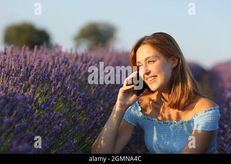 Glückliche Frau, die bei Sonnenuntergang auf einem Smartphone in einem Lavendelfeld spricht Stockfoto