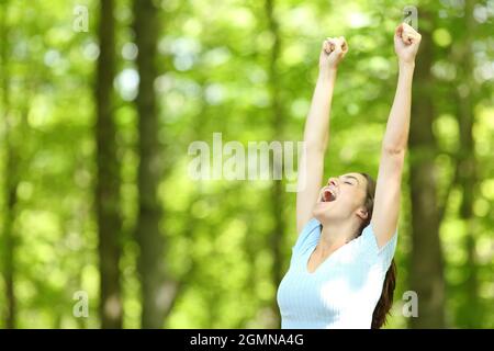 Aufgeregte Frau, die im Sommerurlaub in einem grünen Wald die Arme hebt Stockfoto