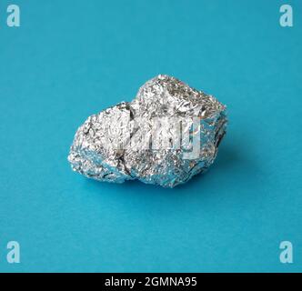 Aluminium. Silberne Aluminiumfolie mit glänzend zerknittertem Aluminiumpapierabfall auf blauem Hintergrund. Die Aluminiumpreise erreichten ein Rekordhoch. Stockfoto