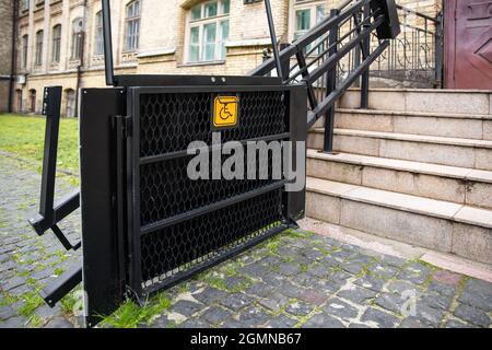 Elektrischer Plattformlift an der Gebäudetreppe für behinderte Menschen mit Rollstuhlschild an der alten Stadtstraße. Aufzug Treppenlift Rampe Mechanismus für Stockfoto