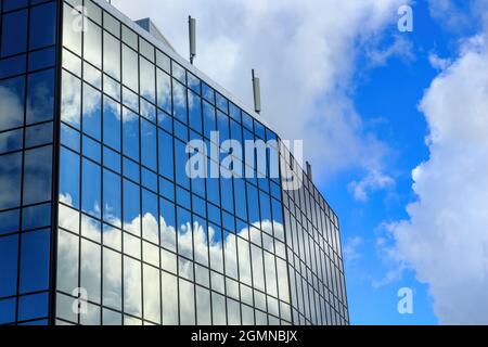 Blauer Himmel und flauschige Wolken spiegeln sich in den Fenstern eines Spiegelglasgebäudes Stockfoto