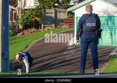Mitglieder der neuseeländischen Polizei in einem Vorort. Einer steht Wache, während ein anderer den Boden durchsucht Stockfoto