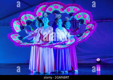 Koreanische Frauen, die unter künstlicher Beleuchtung ein Buchaechum oder traditionellen Fächertanz auf der Bühne vorführen. Sie tragen hanbok-Kleider Stockfoto