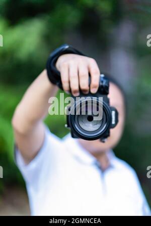 Der asiatische Mann hält die Mittelformatkamera in der Hand und fokussiert, um vor ihm zu fotografieren. Stockfoto