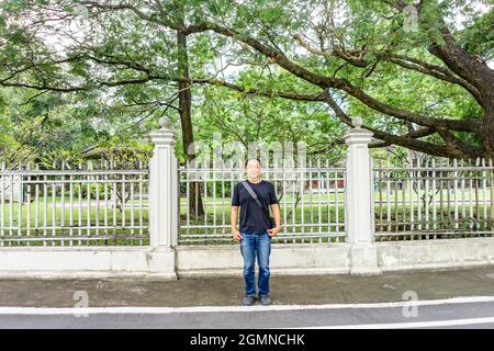 Das Asian Black T-Shirt steht nachmittags vor dem weißen Vintage-Zaun neben der Straße. Stockfoto