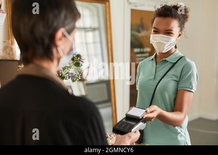 Porträt einer Kundin, die per Smartphone im Blumenladen bezahlt und eine Maske trägt, Kopierraum Stockfoto