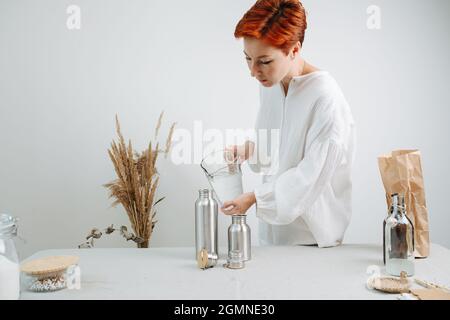 Ingwer kurzhaarige Frau, die Wasser aus einem Krug in eine Metallthermostat gießt. Auf der Mitte eines Tisches. Stockfoto