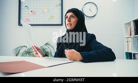 muslimische Geschäftsfrau in Hijab hält Dokument und Stift in einem modernen Büro Stockfoto