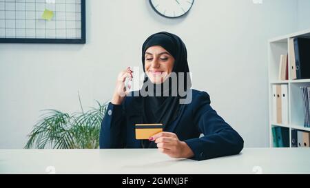 Fröhliche muslimische Geschäftsfrau mit Smartphone und Kreditkarte Stockfoto