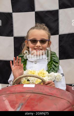 Goodwood, Sussex, Großbritannien. September 2021. Esme Graham winkt aus ihrem Auto vor der schwarz-weißen karierten Flagge. Sie trägt eine Vintage-Sonnenbrille, weiße Overalls, ein breites Lächeln und eine Lorbeer-Girlande, nachdem sie den jährlichen Settrington Cup in ihrem roten Vintage Austin J40 Pedalwagen mit der Nummer 41 gewonnen hat. Ein nostalgisches Rennen für Kinder beim ausverkauften Vintage Goodwood Revival Event 2021. Kredit: Sarnia/Alamy Live Nachrichten Stockfoto