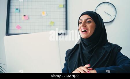 Glückliche muslimische Geschäftsfrau mit Videoanruf auf Laptop im Büro Stockfoto