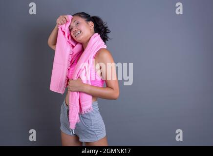 Hübsche Brünette chinesisches Mädchen in Sportswear und wischenden Schweiß mit Handtuch auf grauem Hintergrund. Stockfoto