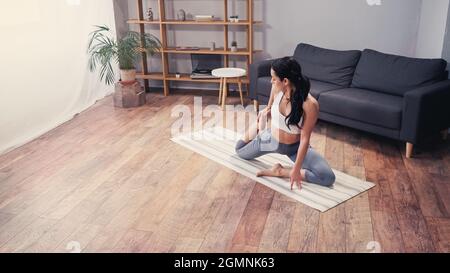 Seitenansicht einer schlanken Sportlerin, die sich im Wohnzimmer dehnt Stockfoto