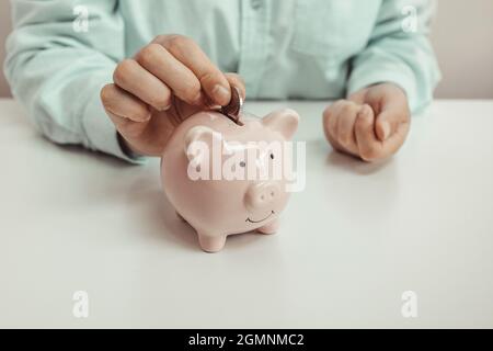 Frau, die Geld in Sparschwein am Tisch gesteckt hat, spart Geld für Zukunftsplan und Pensionskasse Stockfoto