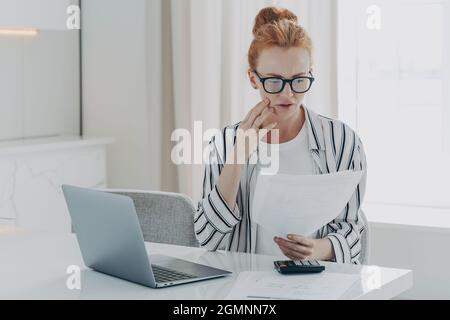 Junge depressive Frau mit finanziellen Problemen, sitzt am Tisch mit Laptop und Rechner Stockfoto