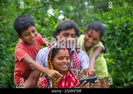 Indische ländliche Eltern und ihre zwei Kinder beim Film auf landwirtschaftlichem Feld Stockfoto
