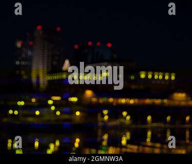Unschärferer Blick auf die Altstadt von Sacramento bei Nacht in der Nähe von Weihnachten von der anderen Seite des Sacramento River, mit Weihnachtslichtern, die auf dem Fluss De Stockfoto