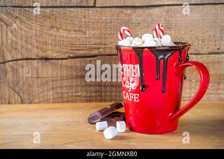 Hausgemachte heiße Schokolade in rotem Becher, mit Mini-Marshallows und Schokoladentropfen, Candy-Cane-Dekor, Kopierraum Stockfoto