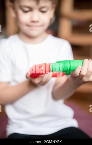 Anti Stress sensorische Pop-Tube Kunststoff-Spielzeug in den Händen des Kindes. Ein kleines glückliches Kind Junge spielt mit einem Poptube Fidget Spielzeug zu Hause. Kinder halten und spielen Stockfoto
