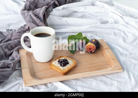 Herbstfrühstück Stillleben. Tasse Kaffee, Feigenfrucht, Brot mit Butter und Marmelade auf Holzbrettchen. Frühstück im Bett, Herbstkost-Konzept. Stockfoto