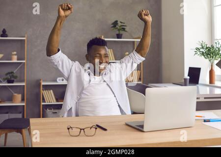Dunkelhäutiger Mann hebt glücklich seine Hände, nachdem er gute Nachrichten erhalten oder das gewünschte Ziel erreicht hat. Stockfoto