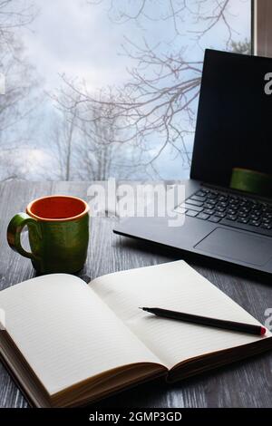 Tasse schwarzen Kaffee auf dunklem Holzhintergrund, Laptop und Notebook in der Nähe geöffnet. Draufsicht