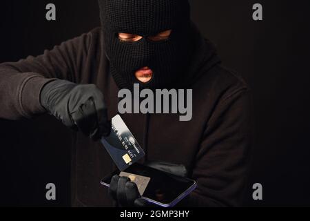 Anonymus Dieb mit Kreditkarte und Telefon. Internet- oder Online-Banking-Hacking Stockfoto