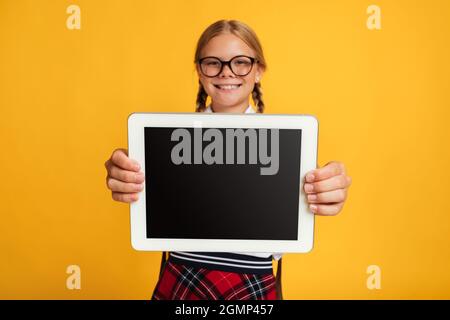 Lächelnde junge blonde Studentin in Brille zeigt Tablet mit leerem Bildschirm, Nahaufnahme, Fernstudium Stockfoto