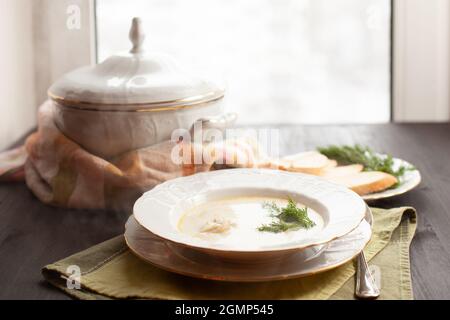 Cremige Fischsuppe mit Lachs, Kartoffeln und Dill auf dem Holztisch neben dem Fenster Stockfoto