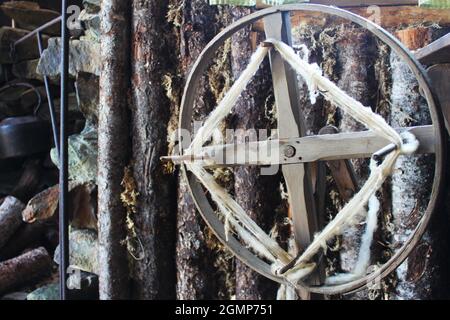 Nahaufnahme eines altmodischen Spinnrads mit Wolle in einer Blockhütte. Über dem Kamin im Hintergrund hing ein Wasserkocher. Stockfoto