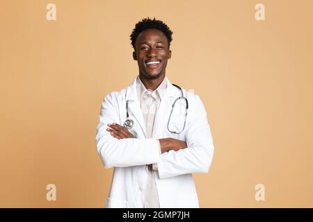 Portrait Of Confident Black Male Doctor In Uniform Posiert Über Beige Hintergrund Stockfoto
