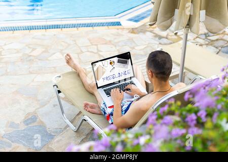 Mann mit Laptop, der sich auf der Sonnenliege am Pool entspannt Stockfoto