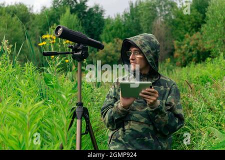 Der Mensch ornitologist sieht sich die Informationen auf der Tablette an oder schreibt sie auf, während er im hohen Gras im Feuchtgebiet steht Stockfoto