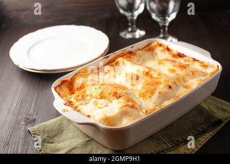 Hausgemachte Lasagne in einer weißen Pfanne auf grünem Küchentuch, zwei Teller und Gläser auf dem Hintergrund Stockfoto