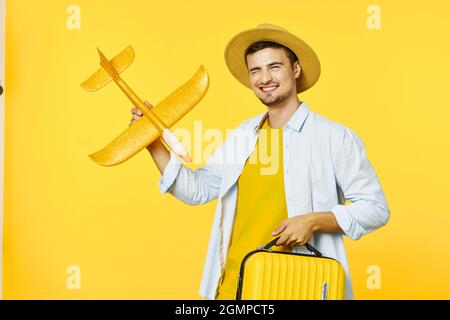 Fröhlicher Mann mit Koffer Flugzeug in der Hand Reise Urlaub gelben Hintergrund Stockfoto