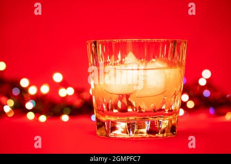 Nahaufnahme eines Glases Whiskey auf den Felsen mit weihnachtslichtern auf rotem Hintergrund - Konzept für weihnachtsgetränke Stockfoto