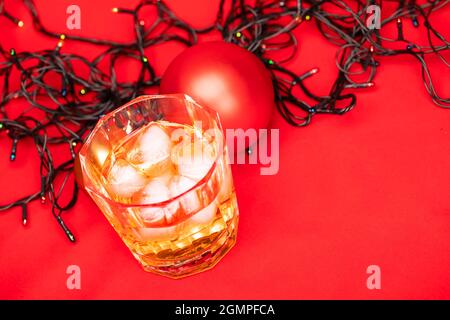 Bleiglas Whiskey mit Eiswürfeln und weihnachtsdekoration auf rotem Hintergrund - weihnachtsgetränk-Konzept Stockfoto