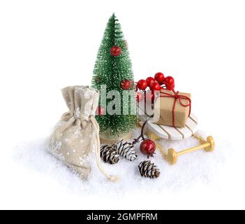 Miniatur-Weihnachtsbaum im Schnee mit Weihnachtsgeschenken auf dem Schlitten isoliert auf Weiß. Stockfoto