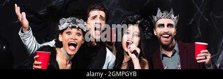 Mann in halloween Make-up gestikiert, während Karaoke mit multiethnischen Freunden auf schwarzem Banner singen Stockfoto