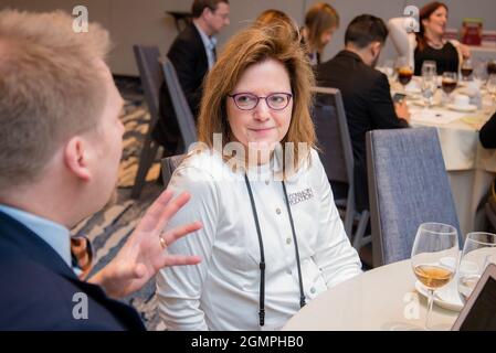 Frau mittleren Alters in weißer Strickjacke hört sich bei einem Networking-Event an Stockfoto