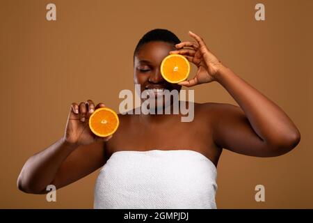 Plus Größe schwarze Frau, die Auge mit Hälften von Orange bedeckt Stockfoto
