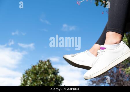 Hängende Füße mit Mädchen-Sneakers, Himmel im Hintergrund, schönes Naturszenario mit Kopierraum Stockfoto