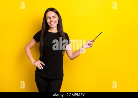 Foto von ziemlich positive Mädchen gesetzt Arm auf Taille aussehen zeigen Bleistift leeren Raum auf gelbem Hintergrund isoliert Stockfoto