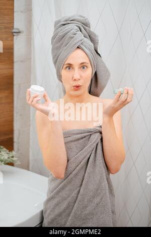 Frau hält ein Glas Gesichtscreme vor dem Badezimmerspiegel. Stockfoto