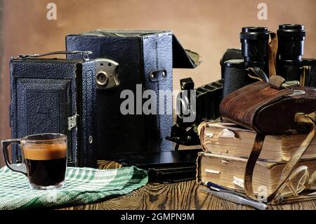 Stapel alter Bücher, Ferngläser, Vintage-Kamera, ausgefranste Ledertaschen auf einem Holztisch Stockfoto