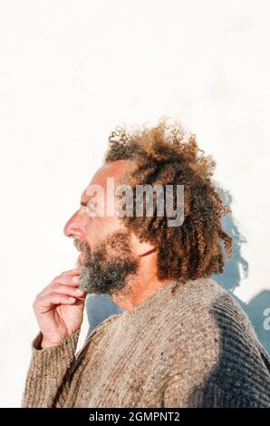 Profil eines nachdenklichen Mannes mittleren Alters mit lockigem Haar, der seinen Bart berührt Stockfoto