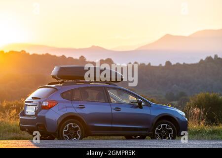 Geländewagen mit Gepäckcontainer auf dem Dach für Geländewagen, der bei Sonnenuntergang am Straßenrand geparkt wird. Roadtrip- und Kurzurlaub-Konzept. Stockfoto