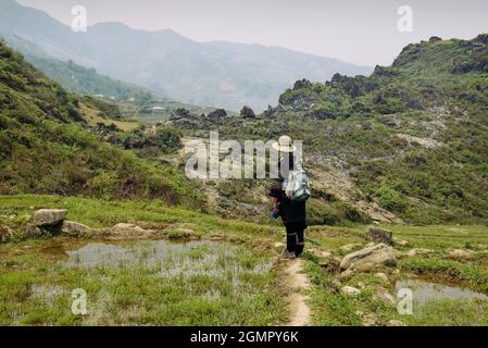 Sapa, Vietnam - 15. April 2016: Frau (Black Hmong), die in nationaler Kleidung durch die Hügel Südostasiens wandert. nordvietnamesische Berge in Stockfoto