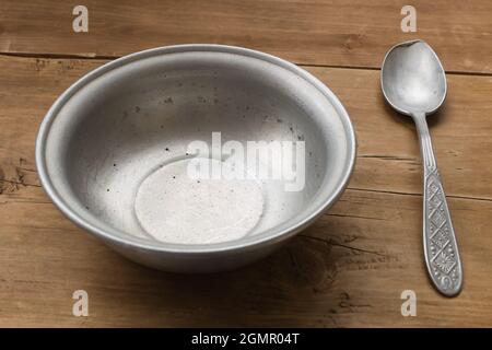 Leere Aluminiumschüssel mit Löffel auf dem alten Holztisch Stockfoto